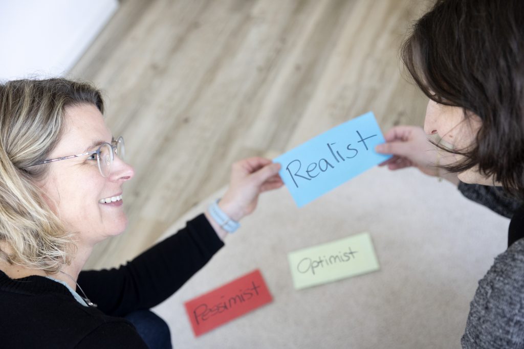 Meike Köster zeigt Coachee eine Karte auf der "Realist" steht